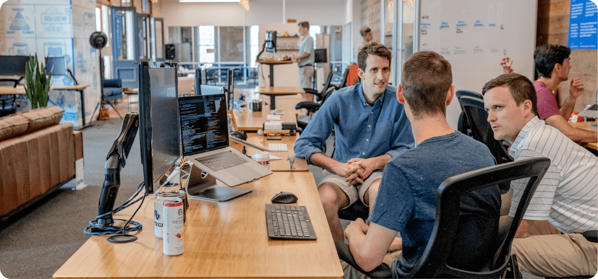 Modern open-plan office with professionals collaborating at wooden desks and computer monitors